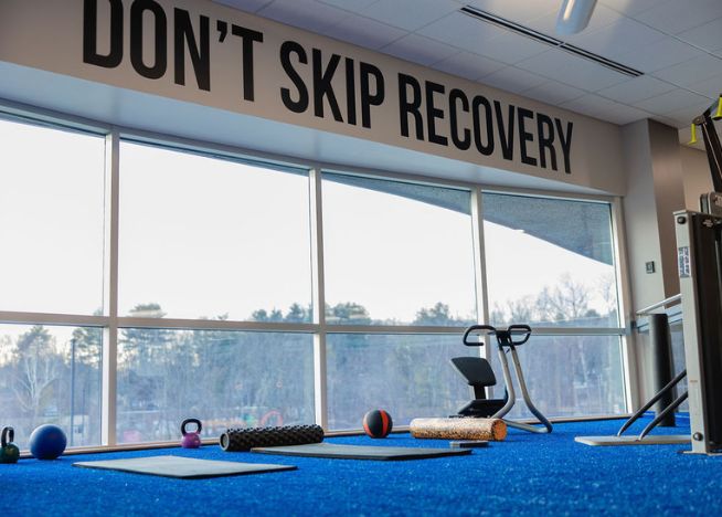 Recovery area at The Workout Club Salem location with mats, foam rollers, and kettlebells under a sign that says Don’t Skip Recovery