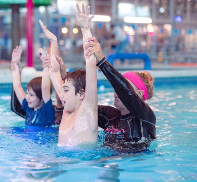 Swim instructor helping kids practice arm strokes during swim lessons at The Workout Club Salem NH indoor pool