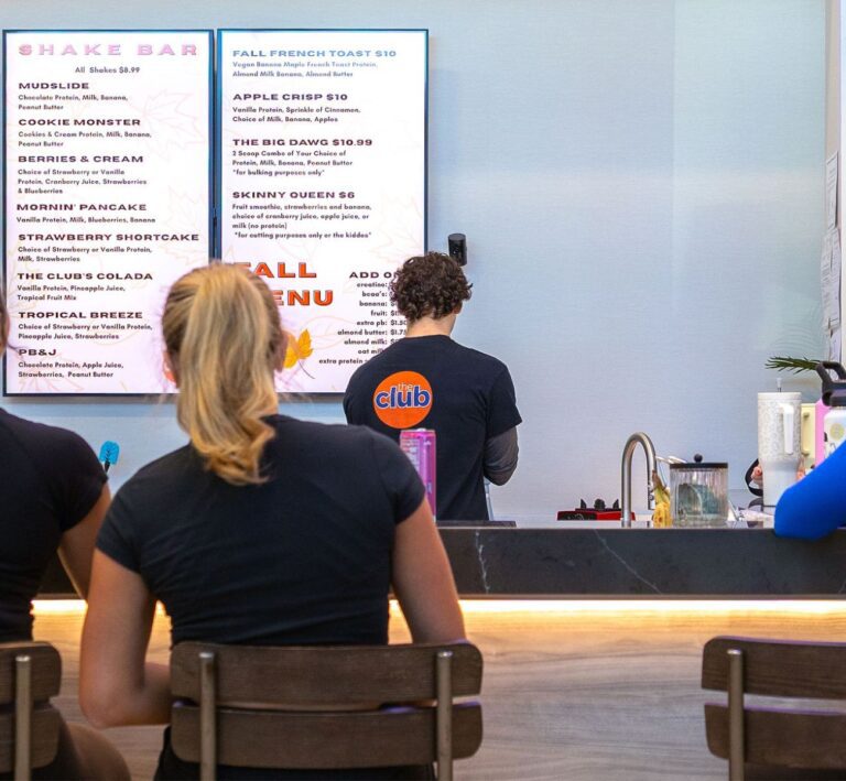 Members sitting at the shake bar at The Workout Club Salem NH looking at the smoothie menu while staff prepares drinks