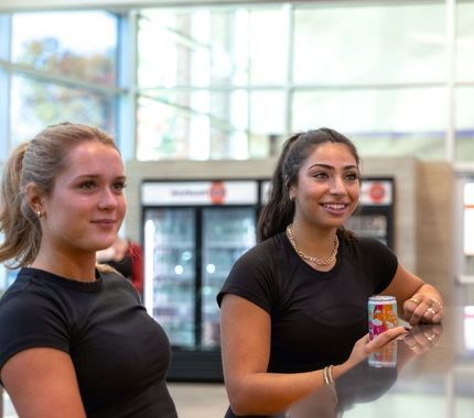 Two members relaxing and chatting at the shake bar counter at The Workout Club Salem NH with drinks and coolers in the background