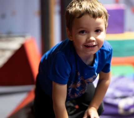 Smiling young boy playing in an indoor obstacle course during The Workout Club’s fun and active kids day camp.