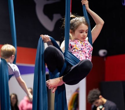 Children practicing aerial silks during an indoor activity at The Workout Club’s youth day camp program.